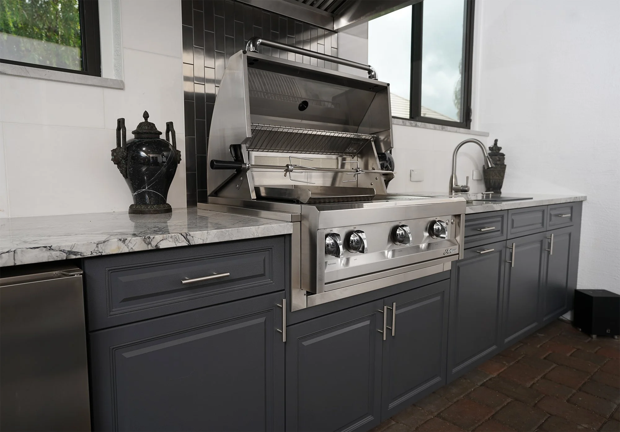 Charcoal raised-panel outdoor cabinets with a built-in grill and marble counter.